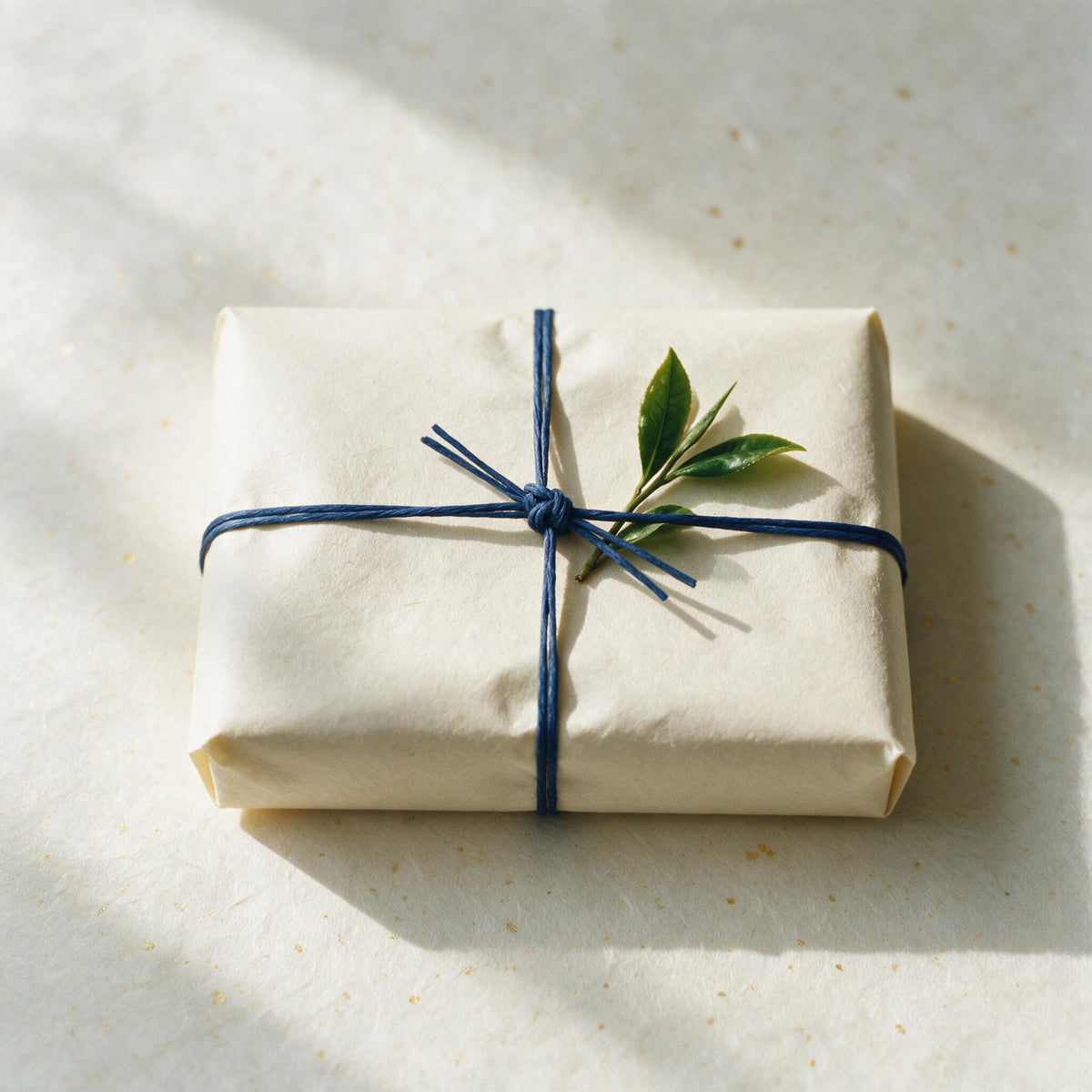 Gift wrapped in cream washi paper tied with an indigo paper cord and a sprig of tea leaf
