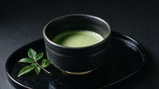 A bowl of thin tea on a black lacquer tray with a sprig of seasonal green