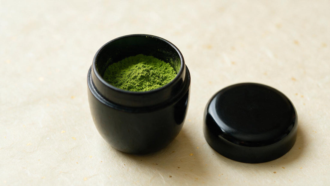 A black natsume tea caddy with its lid lifted, matcha inside