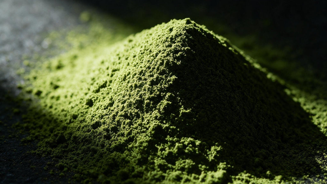 A mound of stone-milled matcha powder, vivid green and finely textured, lit from one side on dark stone