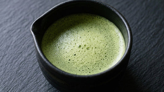A black tea bowl of whisked thin matcha held on a dark table, seen from above