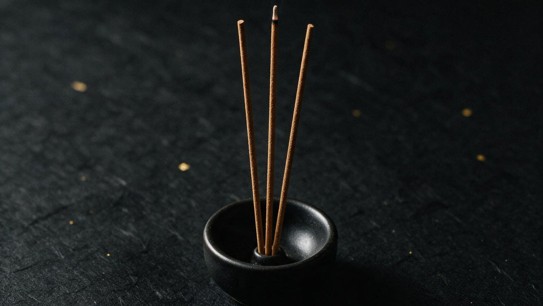 Three Japanese incense sticks standing in a small black ceramic holder on dark paper