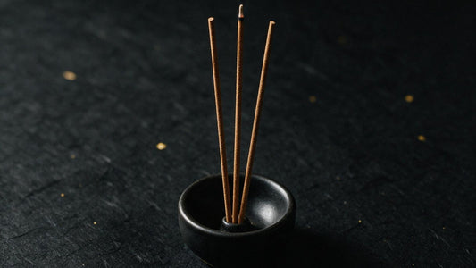 Three Japanese incense sticks standing in a small black ceramic holder on dark paper