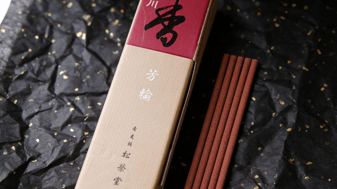 A box of Shoyeido Horikawa incense with five reddish-brown sticks laid beside it on black paper flecked with gold