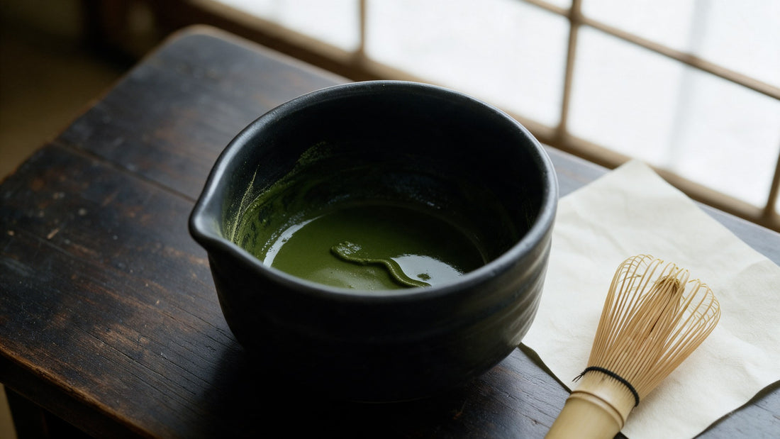 A shallow pool of thick kneaded matcha in a black bowl, opaque and dark jade with the ridge left by the whisk still standing