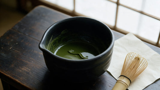 A shallow pool of thick kneaded matcha in a black bowl, opaque and dark jade with the ridge left by the whisk still standing