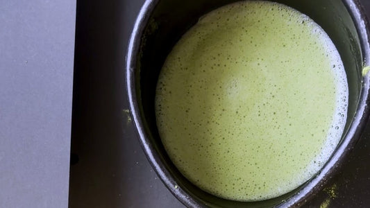 A bowl of whisked matcha seen from directly above, the surface still holding fine foam