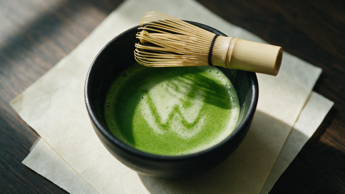 Freshly whisked matcha in a black bowl with the whisk laid across the rim