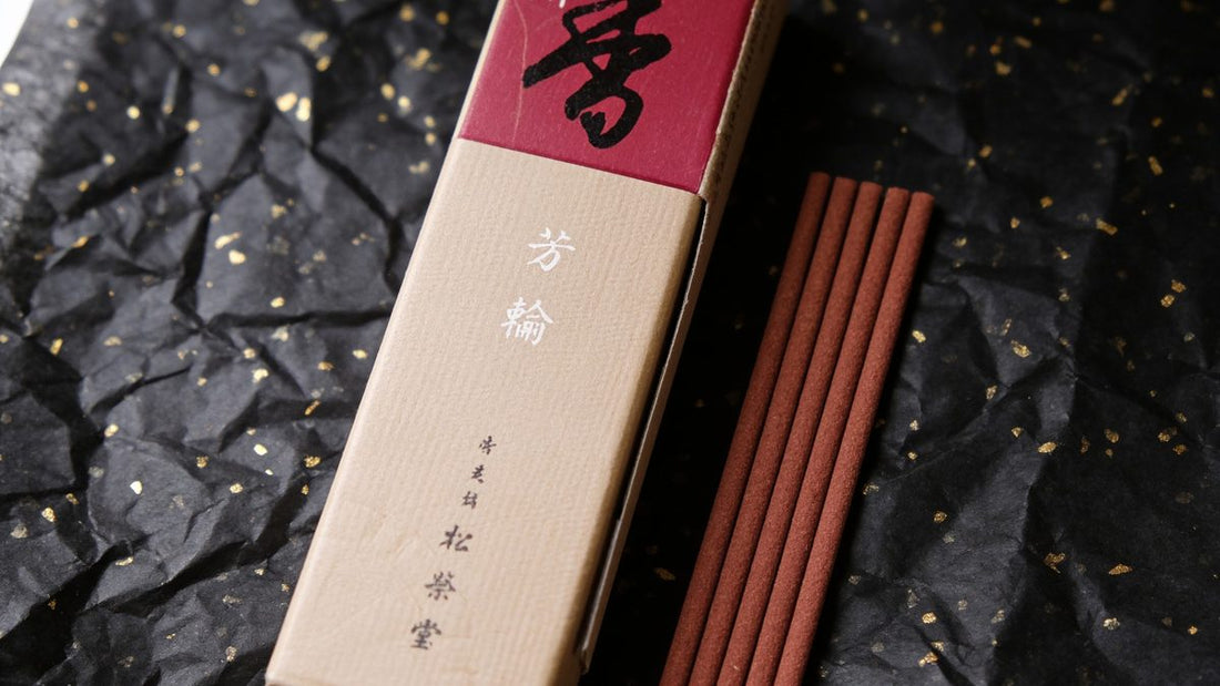 A box of Shoyeido incense from the Horin series, opened beside five slender reddish-brown sticks on black paper flecked with gold