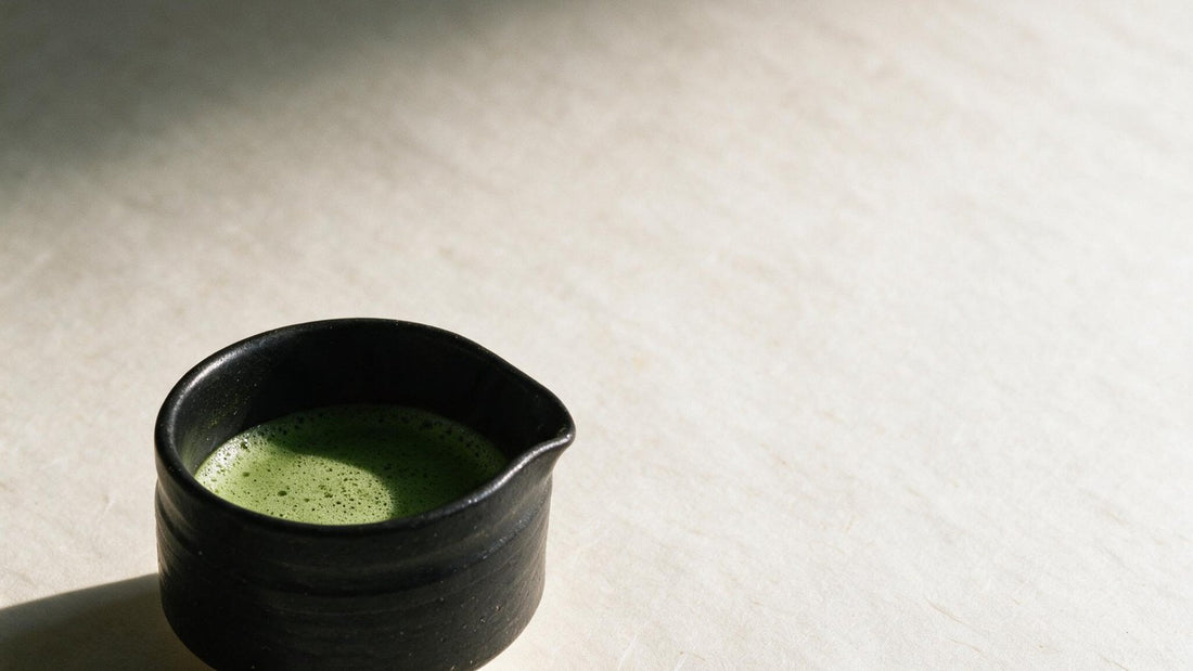 A small black tea bowl holding whisked matcha, resting on a pale linen cloth in low sunlight