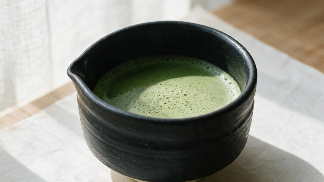 A black Mino-yaki chawan with a small pouring lip, holding a bowl of freshly whisked thin matcha