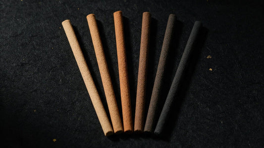 Japanese incense sticks of several colors laid side by side on dark paper, each a solid stick with no bamboo core