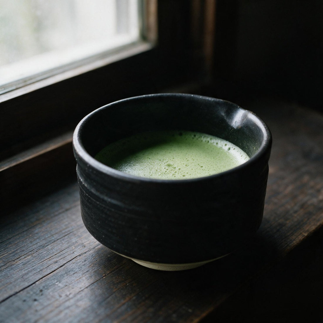 A bowl of whisked matcha by a window in soft autumn light