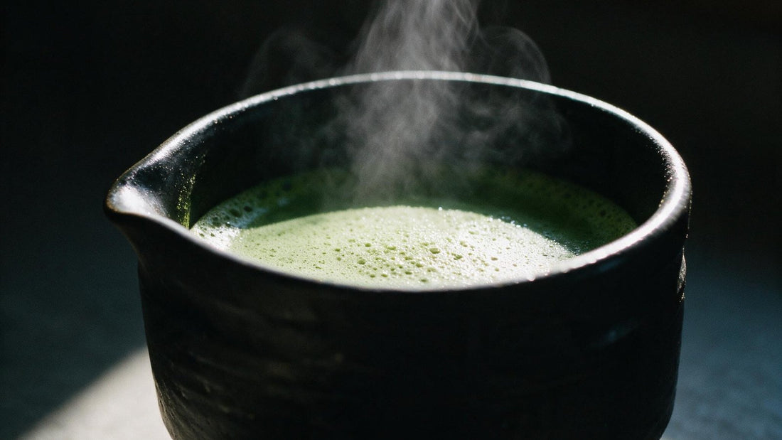 Steam rising from a black bowl of freshly whisked matcha in low window light
