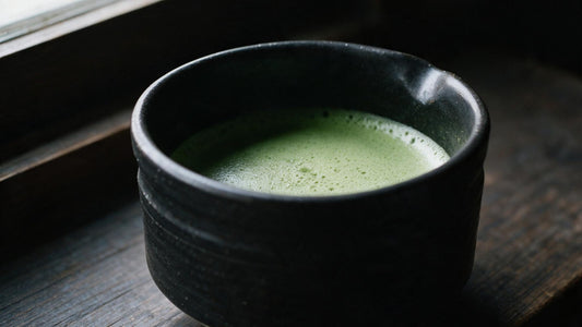 A black Mino-yaki tea bowl of thin matcha resting on a wooden sill in window light