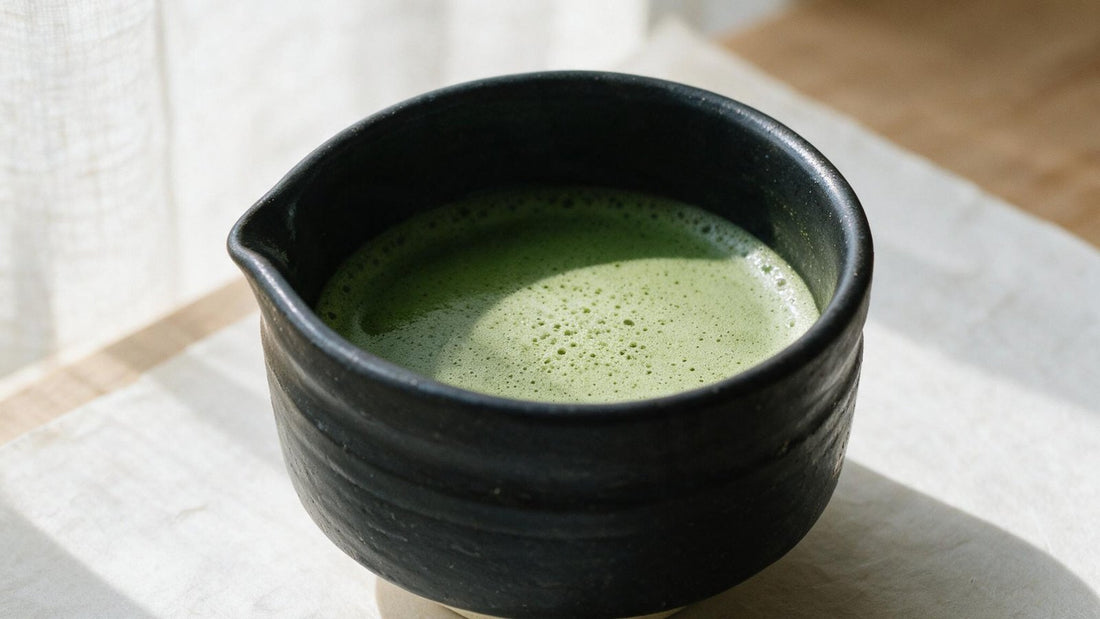 A black Mino-yaki tea bowl of whisked matcha on a linen cloth, lit from a window