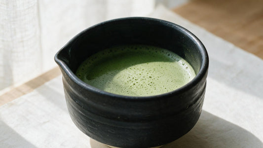 A black Mino-yaki tea bowl of whisked matcha on a linen cloth, lit from a window
