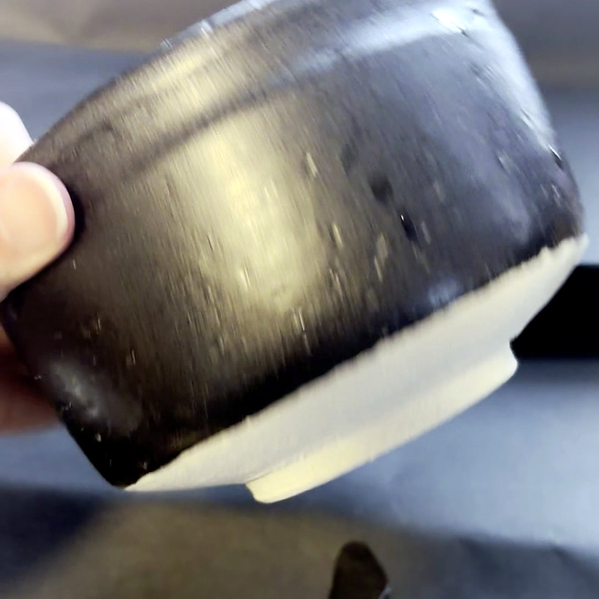 The chawan tilted to show the glaze stopping above the unglazed foot