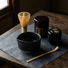 The five pieces of the Complete Tea Set: the black Mino-yaki bowl with its pour spout, a Takayama bamboo whisk, the earlier brown matcha sifter (it now comes in glossy black), a maki-e tea caddy and a flat bamboo scoop