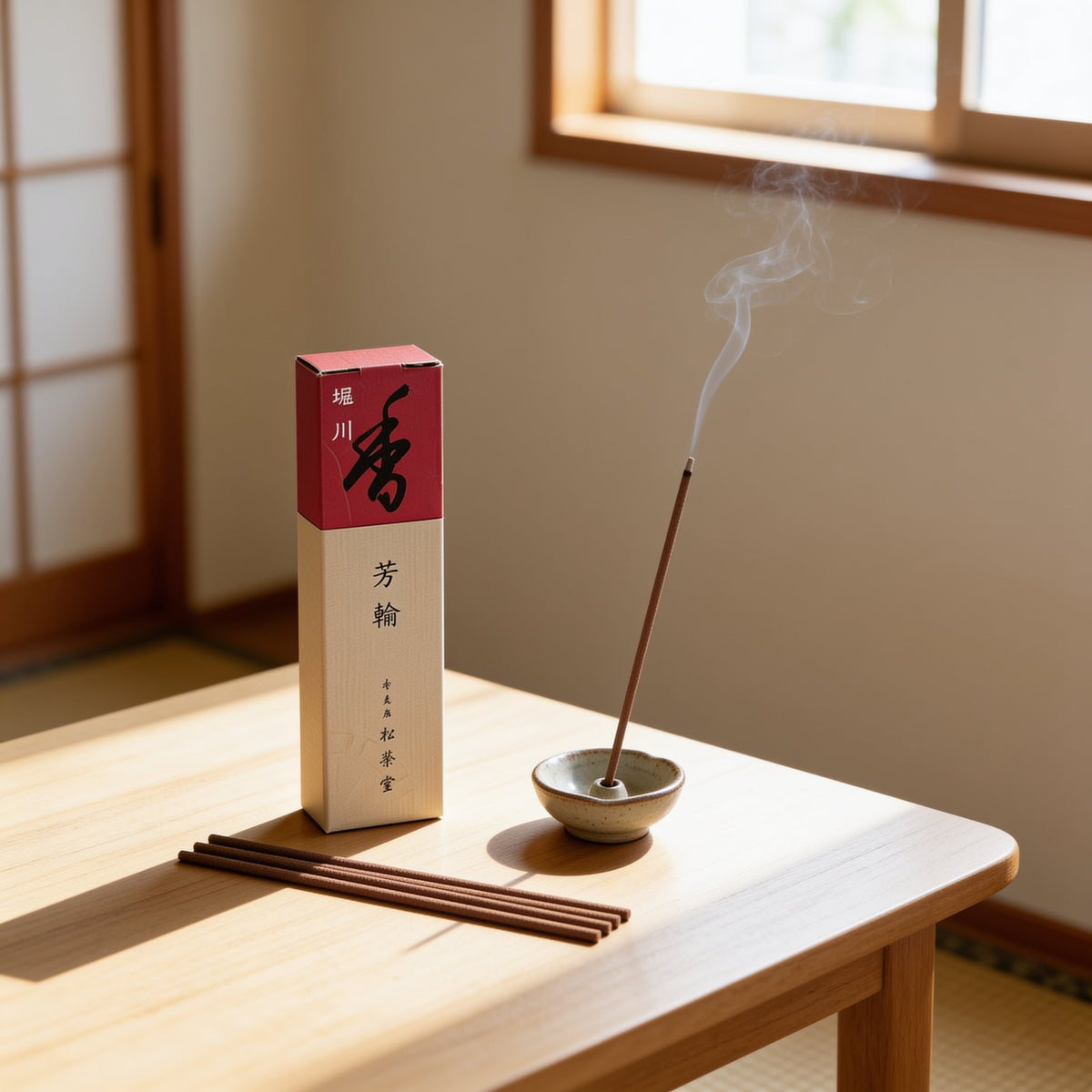 A box of Horin Horikawa incense from Shoyeido beside a lit stick in a small holder on a table by a shoji window