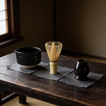 The kusenaoshi beside a black spouted matcha bowl and a bamboo whisk, to show its size