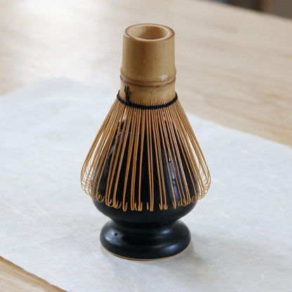A bamboo matcha whisk resting head-down over the kusenaoshi, tines splayed around the dome