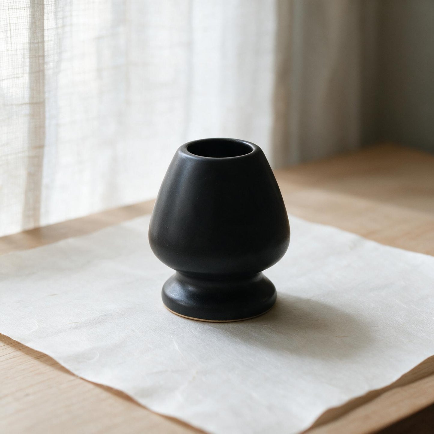 Matte black ceramic kusenaoshi, a matcha whisk shaper, on washi paper