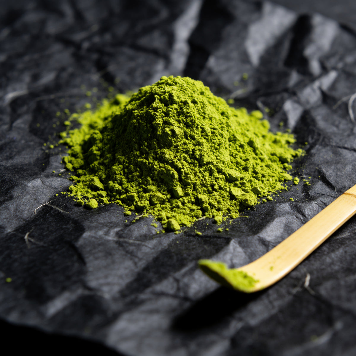 A small mound of bright green matcha powder with a bamboo tea scoop on dark washi paper (AI-generated image)