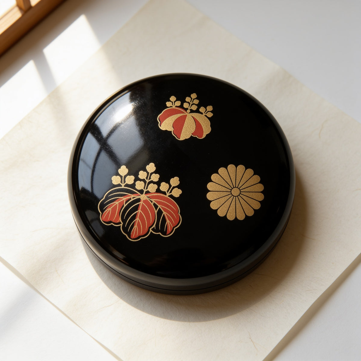 The lid of the natsume seen from above: two paulownia crests in gold and vermilion and one gold chrysanthemum crest on glossy black