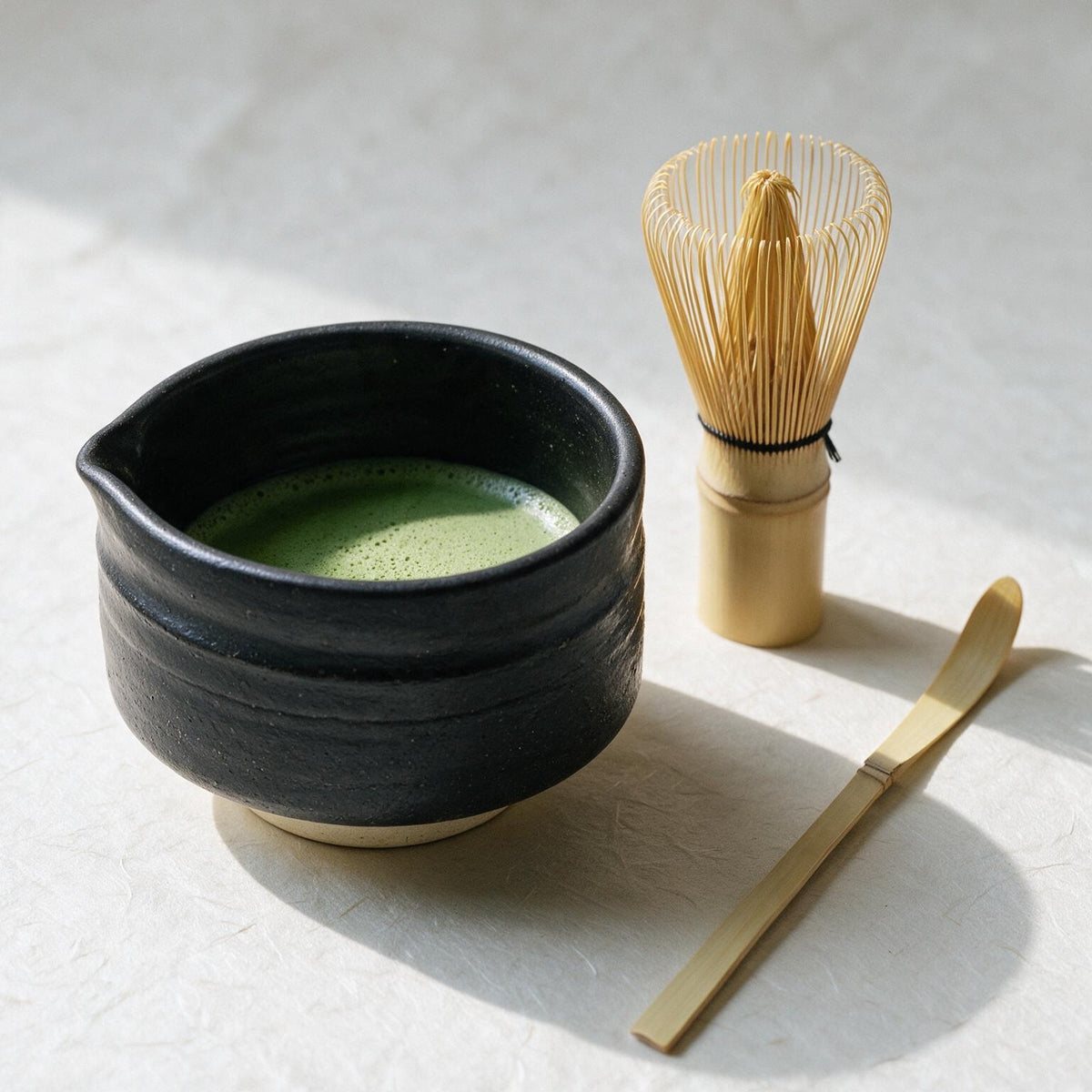 The set just after use: the low wide Mino-yaki bowl of whisked thin tea, the chasen standing beside it, and the flat bamboo chashaku