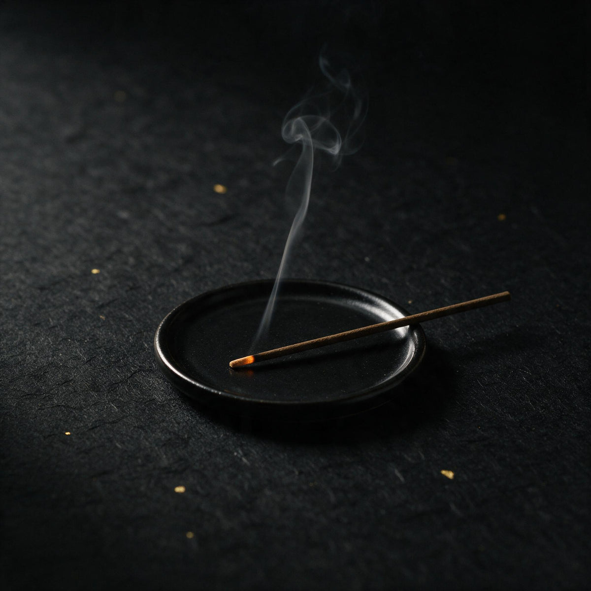 A single incense stick burning in a small black dish, a thread of smoke rising