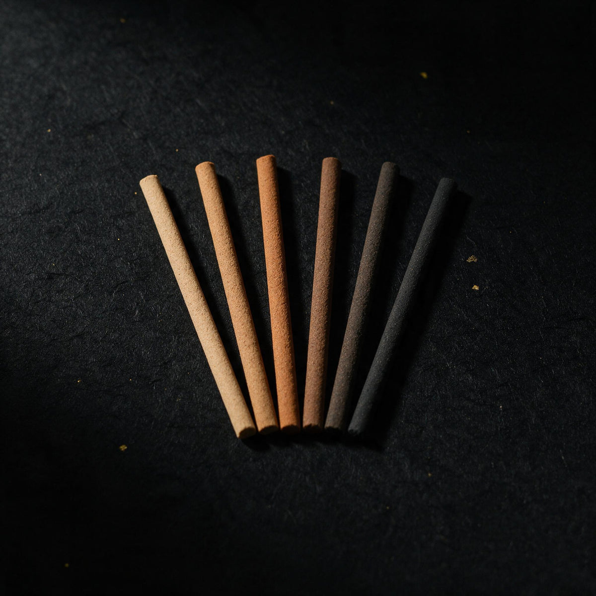 Six incense sticks in different shades laid side by side in a fan on black washi